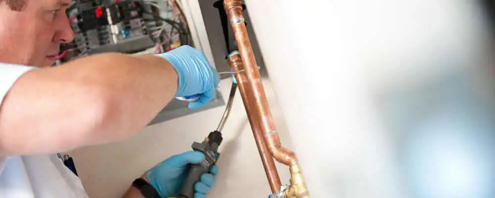 Water heater repair technician testing copper pipe connections and controls in Lynchburg, VA